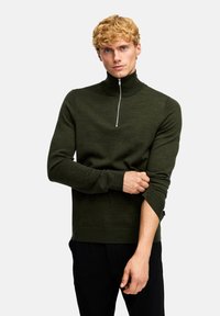 Donkergroen, aansluitend sweater met een hoge kraag en zilveren ritssluiting. Ribbelmanchetten en -zoom zorgen voor textuur op de zachte brei stof.