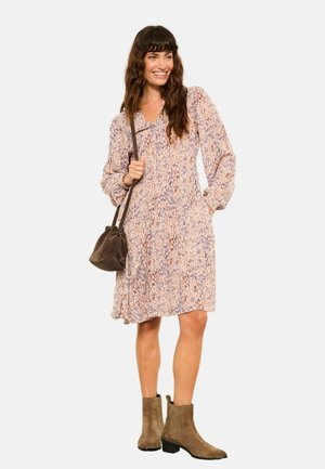 Kleid mit Blumenmuster in helllila und Creme, tailliert, mit langen Ärmeln, kombiniert mit einer dunkelbraunen Tasche und Stiefeletten.