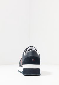 Granatowe sneakersy z cholewką ze zamszu i skóry, biała środkowa podeszwa oraz czerwona akcentująca pasek. Posiadają logo i teksturowany zapiętek. Zamknięty tył.