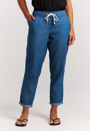 Hellblaue Denim-Jogginghosen mit elastischem Bund, verstellbarem Kordelzug und Seitentaschen. Die Hosenbeine sind an den Knöcheln umgeschlagen.