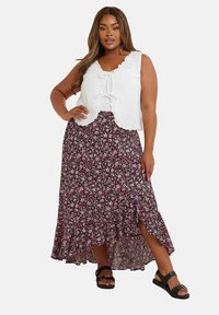 Vit texturerad linne med knyt fram, tillsammans med en svart blommig maxikjol med rosa och vita blommor och en sidofåll. Svarta sandaler.