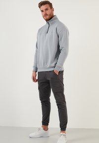 Sudadera de forro polar gris claro con media cremallera, que presenta un cuello y puños acanalados, combinada con pantalones cargo oscuros ajustados y zapatillas blancas.