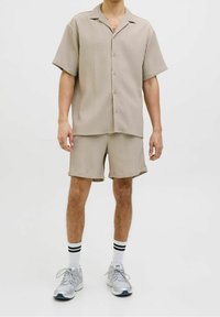 Beige gestreept shirt met korte mouwen en kraag, gecombineerd met bijpassende korte broek. Draagt witte enkelsokken met zwarte strepen en grijze sneakers.