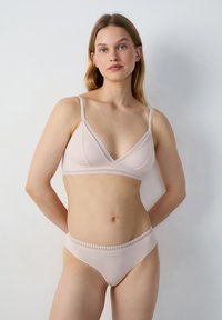Bralette rose clair avec un design triangulaire, des détails en dentelle et des bretelles réglables, associée à un slip bikini assorti avec un détail en dentelle similaire.