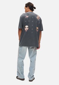 Grå oversized T-shirt med flere portrætter og teksten "CROSSROADS" på ryggen. Stylet med lyseblå jeans med farvepletter.