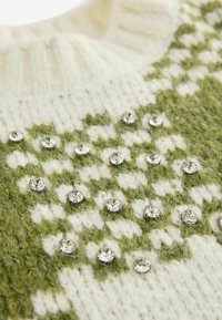 Sweter z dzianiny w kremowo-zielony geometryczny wzór, zdobiony wtopionymi przezroczystymi cyrkoniami oraz teksturowanym kołnierzem.