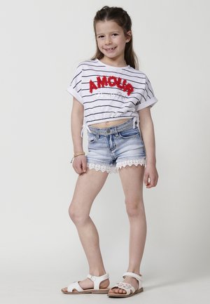 Cropped top blanco a rayas con el texto rojo "AMOUR", combinado con pantalones cortos de mezclilla azul claro con encaje y sandalias blancas.
