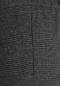 Woven grey and black plaid fabric featuring a textured surface. Includes subtle detailing and a single pocket.