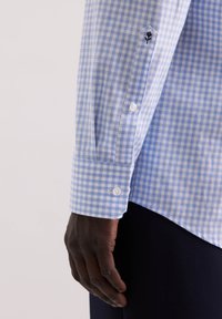 Camicia a quadretti blu e bianca con polsini a bottoni, caratterizzata da un piccolo dettaglio di un fiore ricamato in nero sulla manica. Materiale in cotone.
