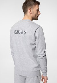 Szara bluza z długim rękawem, okrągłym dekoltem oraz żebrowanymi mankietami i dołem. Na plecach znajduje się haftowane "1948" w ciemnoniebieskim kolorze. Miękka tekstura materiału.