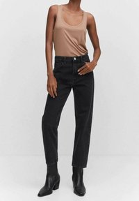 Vaqueros de mezclilla negros con un diseño de pierna recta, cintura alta, cinco bolsillos y cierre de botón, combinados con una camiseta sin mangas color marrón claro y botas de tacón negras.