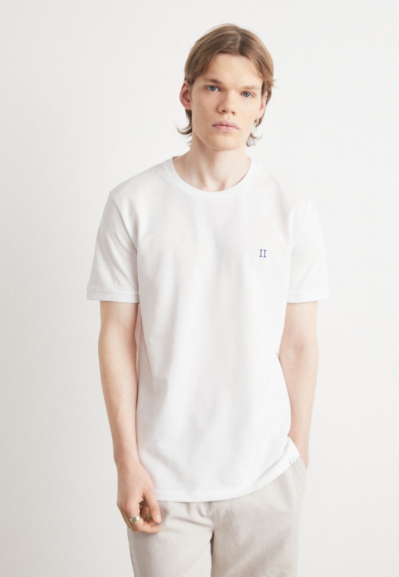 Tricou alb din bumbac, cu decolteu rotund, mâneci scurte și un mic detaliu brodat "II" de culoare albastră pe partea stângă a pieptului. Textură netedă.