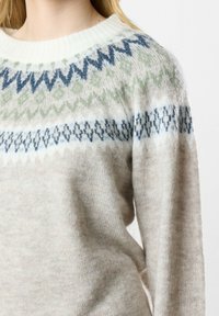 Strickpullover in Beige und Creme mit grünen und blauen geometrischen Mustern auf der Brust. Weiche Textur mit rundem Ausschnitt.