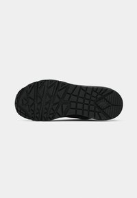 Semelle de chaussure en caoutchouc noir avec des motifs géométriques de la bande de roulement comprenant des triangles et des carrés sur un fond uni clair.