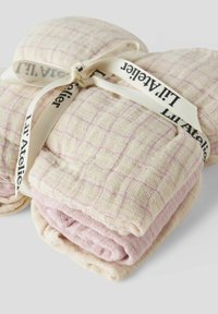 Cotton muslin blankets in cream with pastel pink accents, featuring a grid pattern. Tied with a branded ribbon for presentation.