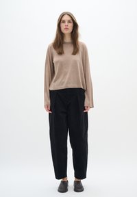 Maglietta beige a maniche lunghe con vestibilità rilassata, abbinata a pantaloni neri in corda a vita alta e scarpe scure slip-on. Design minimalista, tessuto testurizzato.