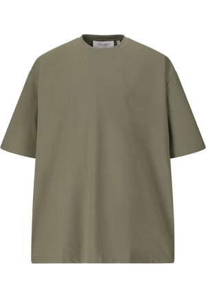 Ung mand går, iført en olivengrøn T-shirt, sorte bukser og hvide sneakers mod en ensfarvet hvid baggrund.