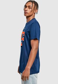Mørkeblå bomulds t-shirt med et stort orange og blåt grafisk print på forsiden. Korte ærmer og en klassisk rund halsudskæring.
