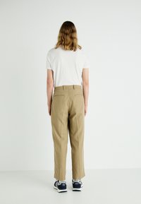 Khaki tapered trousers with a high waistband, two back pockets, and a smooth texture, paired with a plain white t-shirt and sneakers.