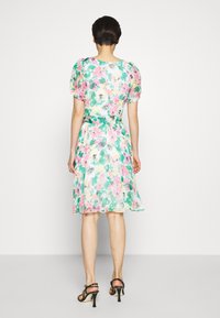 Blumenkleid mit grünem, pinkem und gelbem Muster, Puffärmeln und einer betonten Taille. Leichter Stoff mit fließendem Schnitt.