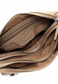 Interior de bolsa de cuero beige con múltiples compartimentos y bolsillos con cremallera. Forro de tela texturizada y detalles de cremallera suave.