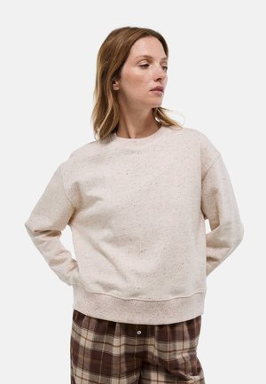 Sweatshirt rose clair avec un col rond et des manches longues, présentant une texture mouchetée. Associé à un pantalon à carreaux marron.