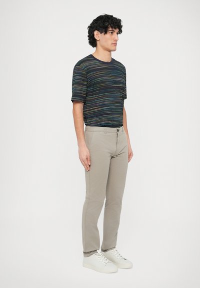 Granatowy t-shirt w paski z wielokolorowymi poziomymi liniami, zestawiony z jasnobeżowymi spodniami i białymi tenisówkami. Luźny fason i krótkie rękawy.