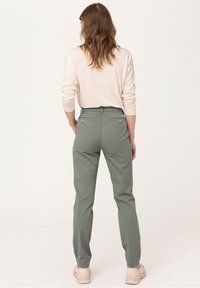 Zelené slim fit kalhoty vyrobené z lehkého materiálu, s zadními kapsami a zipovým zapínáním. V kombinaci se krémovým topem.