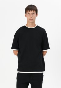 Schwarzes T-Shirt mit kurzen Ärmeln, kontrastierendem weißen Kragen und Bündchen. Hergestellt aus festem Stoff, zeichnet sich durch einen entspannten Sitz und ein minimales Design aus.