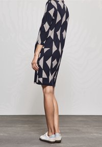 Robe longueur genoux bleu marine à motif géométrique gris. Manches trois-quarts et tissu doux. Associée à des baskets blanches et bleu clair.