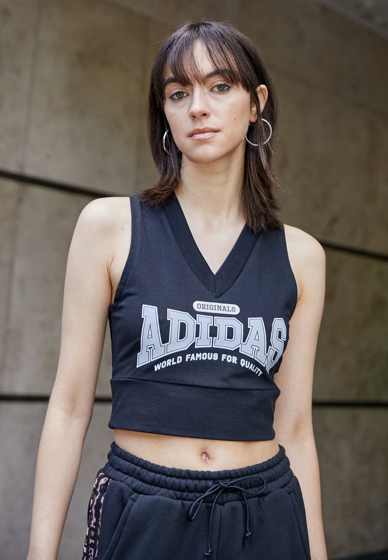 Fekete, V-nyakú, cropped tank top fehér "ADIDAS" logóval, fekete jogger nadrággal, amelynek derékban húzózsinór található.