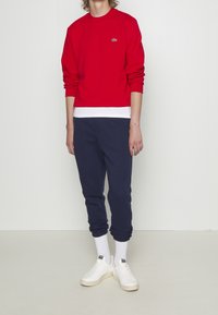 Punainen pitkähihaisen puuvillainen collegepaita yhdistettynä tummansinisiin verkkarihousuihin. Asun täydentävät valkoiset matalavartiset sukat ja valkoiset tennarit.