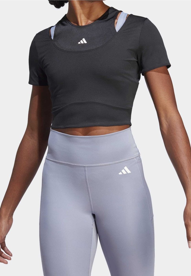 Svart kortärmad croptop med smal passform och rund halsringning. Kombinerad med ljusgrå högmidjade leggings som har en vit logotypdetalj.