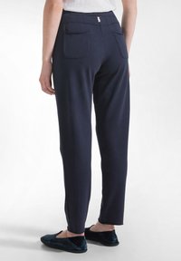 Tmavě modré elastické kalhoty s hladkou texturou, s dvěma zadními kapsami a přiléhavým pasem. Označené malým štítkem na zadní straně.