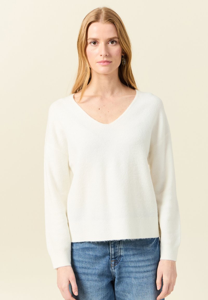 Witte, gestructureerde trui met een V-hals en lange mouwen, met een iets verkorte zoom. Gecombineerd met blauwe denim jeans.