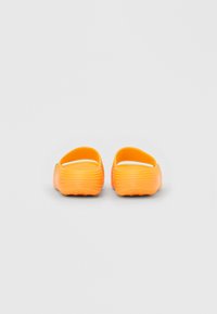 Lyse orange slip-on sandaler med teksturerede såler, vist bagfra på en ensfarvet lys baggrund.