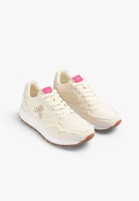 Sneaker beige con tomaia in tela testurizzata, accenti rosa sulla linguetta e suola in gomma bianca con un motivo battistrada marrone. Logo a forma di teschio sul lato.