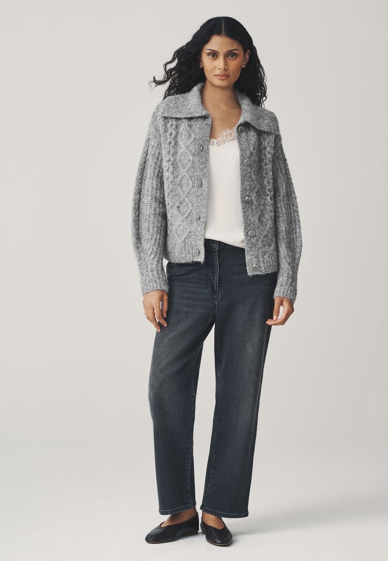 Cardigan grigio lavorato a maglia con motivo a rombi, vestibilità oversize e collo ampio. Abbinato a jeans scuri a gamba dritta e scarpe slip-on nere.