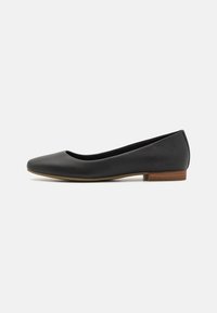 Bailarinas de cuero negro con punta redondeada, diseño minimalista, tacón bajo y un pequeño detalle marrón en el talón. Logo en la parte trasera.