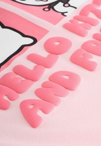 Tappeto in peluche rosa con lettere rialzate di morbido rosa che formano le parole "CIAO" e "E" su uno sfondo rosa chiaro con contorni neri.