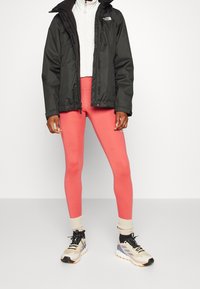 Veste noire imperméable, polaire zippée blanche, leggings roses et baskets beiges avec des accents noir et bleu ciel. Conception texturée et ajustée.