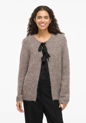 Ljusbrun, fluffig stickad cardigan med rund hals, öppen fram och svart bandknut. Långa ärmar med ribbade fållar.