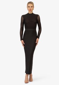 Robe noire au design ajusté, avec de longues manches transparentes et un col haut. Présente une texture lisse et une silhouette droite jusqu'aux chevilles.