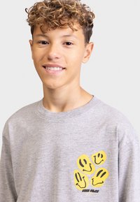 Graues Langarmshirt mit einem Grafikdesign, das vier gelbe Handabdrücke und lächelnde Gesichter im linken Brustbereich zeigt. Aus Baumwolle, lässige Passform.