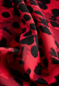 Crvena tkanina s izrazitim crnim uzorkom leoparda, glatke teksture i padajućeg izgleda koji naglašava njen fleksibilan dizajn.