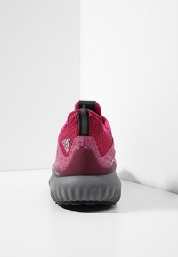 Chaussure de sport rose avec un upper en mesh respirant, semelle grise rembourrée et accent noir au talon avec un logo. Vue arrière affichée.