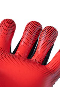 Guanto rosso con accenti e motivi neri a pois. Realizzato in un materiale liscio e lucido, presenta una superficie di presa testurizzata e un tessuto nero sul polso.