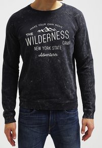 Felpa nera con tessuto strutturato, scollatura rotonda e maniche lunghe. Grafica bianca "Wilderness Camp New York State" con design di montagna.