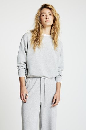 Felpa grigia con vestibilità comoda, scollo rotondo e maniche lunghe. Abbinata a pantaloni della tuta coordinati con vita elastica e coulisse.