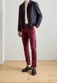 Giubbotto bomber navy, camicia leggera, pantaloni slim-fit bordeaux e mocassini neri con dettagli in metallo. Texture morbide, design moderno.